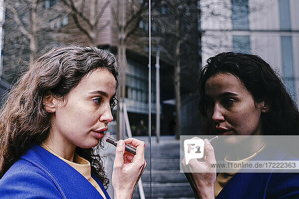 Junge Geschäftsfrau trägt Lippenstift auf und betrachtet ihr Spiegelbild