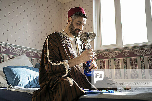 Man doing preparation of hookah while sitting on bed at home