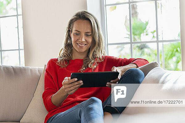 Lächelnde Frau mit digitalem Tablet auf der Couch