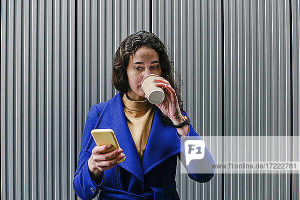 Unternehmerin trinkt Kaffee und benutzt ihr Smartphone vor einer Wand