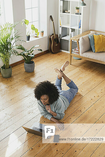 Junge Frau benutzt einen Laptop  während sie auf dem Boden im Wohnzimmer liegt