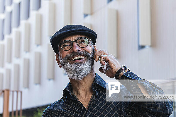 Lächelnder Mann  der wegschaut  während er mit einem Mobiltelefon in der Stadt spricht