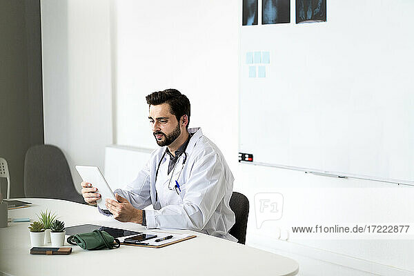 Handsome male doctor using tablet sitting at desk in hospital