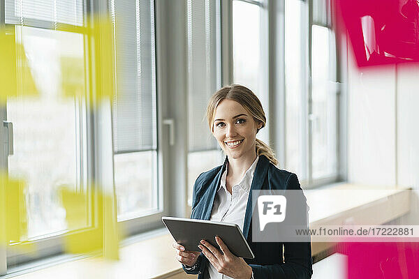 Lächelnde weibliche Fachkraft mit digitalem Tablet im Büro stehend