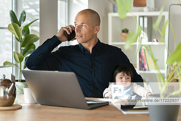 Vater telefoniert mit seinem Smartphone  während er sein kleines Mädchen zu Hause hält