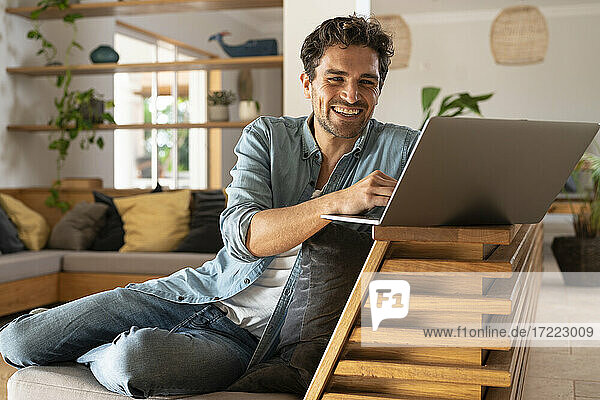 Glücklicher männlicher Freiberufler  der einen Laptop benutzt  während er zu Hause sitzt
