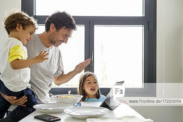 Vater und Sohn winken mit der Hand während eines Videoanrufs über ein digitales Tablet durch ein Mädchen zu Hause