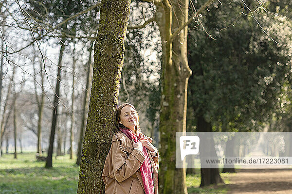 Lächelnde Frau lehnt an einem Baum im Park