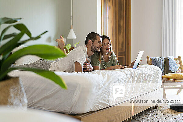 Junges Paar  das einen Laptop benutzt  während es zu Hause im Schlafzimmer auf dem Bett liegt