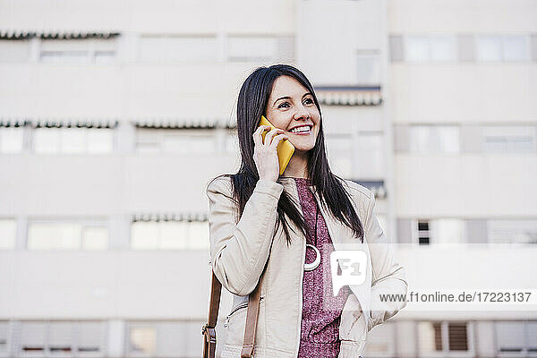 Lächelnde schöne Frau  die wegschaut  während sie mit einem Mobiltelefon spricht