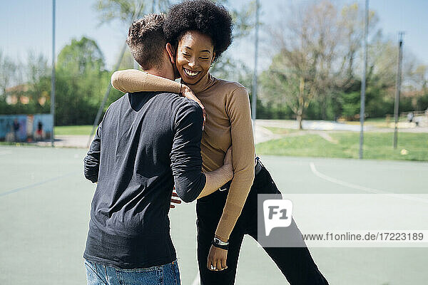 Lächelnde Afro-Frau  die ihren Freund auf dem Sportplatz umarmt