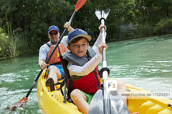 Cute boy and father canoeing in lake during vacation