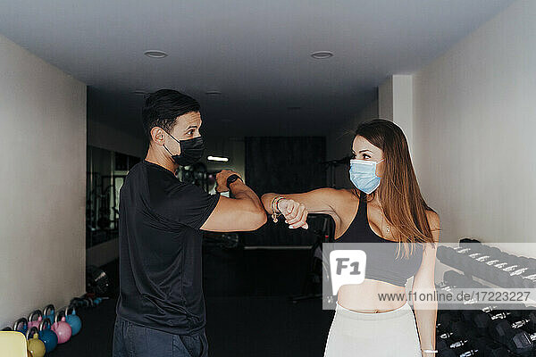 Sportler mit Schutzmaske grüßen mit Ellenbogenstoß im Fitnessstudio