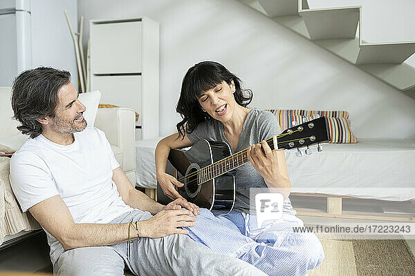 Reifer Mann sieht Frau beim Gitarrenspielen zu Hause an