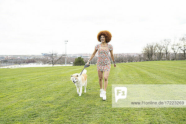 Lächelnde Frau hält Leine beim Spaziergang mit Hund im Park
