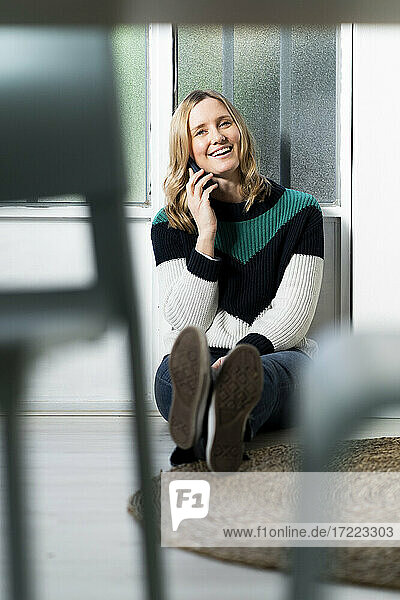 Blonde Frau lächelt  während sie zu Hause mit dem Handy telefoniert