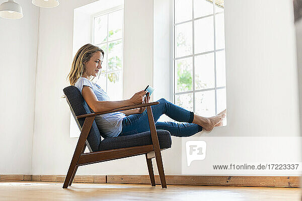 Mid adult woman using digital tablet while sitting on armchair at home
