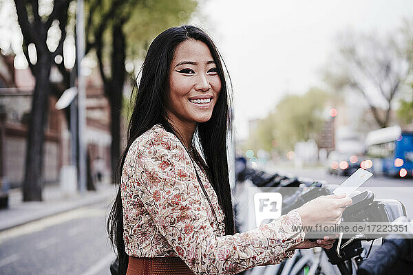Lächelnde Frau  die in der Stadt mit Kreditkarte ein Fahrrad mietet