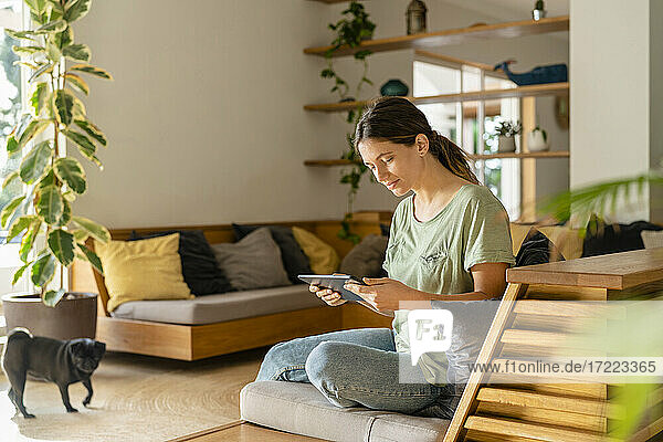 Junge Frau benutzt ein digitales Tablet  während sie zu Hause auf dem Sofa sitzt