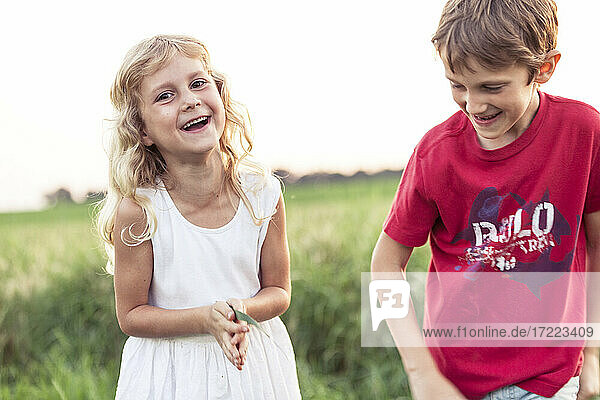 Fröhliches süßes Mädchen  das neben seinem Bruder auf einer grünen Wiese steht