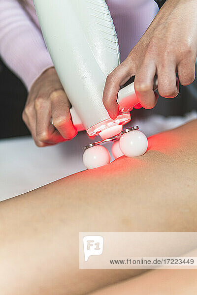 Die Hände einer Kosmetikerin massieren die Beine einer jungen Frau mit einem Lasermassagegerät