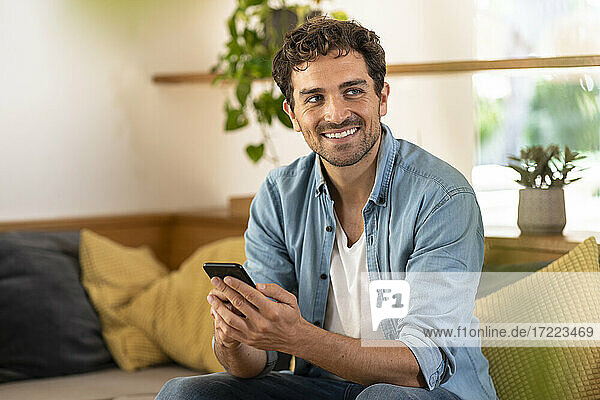Smiling handsome man holding smart phone while sitting on sofa