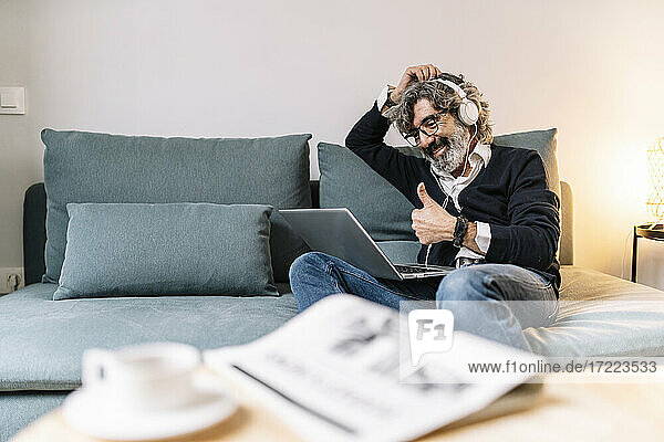Lächelnder Mann zeigt Daumen nach oben während eines Videogesprächs auf dem Laptop zu Hause