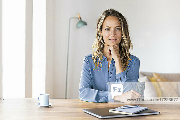 Schöne Geschäftsfrau mit Hand am Kinn sitzt am Schreibtisch im Büro zu Hause