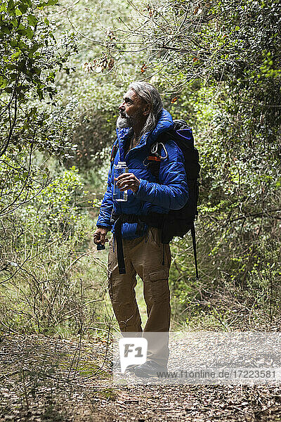Male explorer holding water bottle while looking at plants in forest during weekend