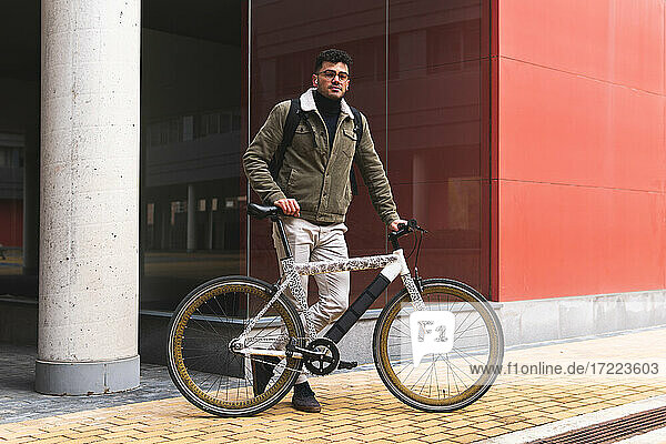 Gutaussehender Geschäftsmann mit Fahrrad auf dem Fußweg stehend