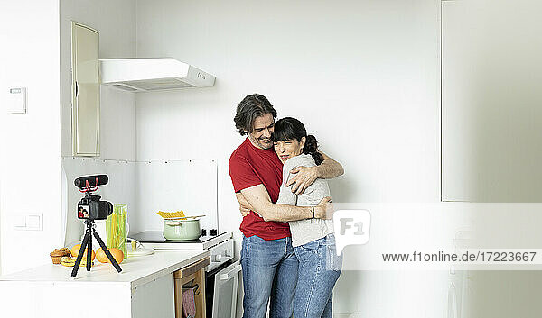 Paar umarmt sich beim Vlogging in der Küche zu Hause