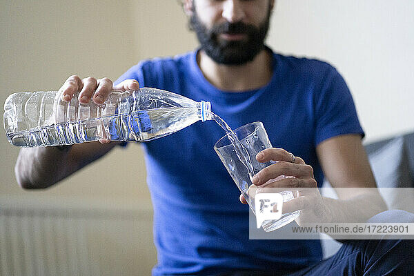 Durstiger junger Mann gießt zu Hause Wasser in ein Trinkglas