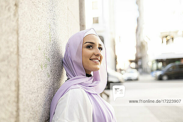 Schönes Teenager-Mädchen im Hijab schaut weg  während sie an einer Mauer in der Stadt steht