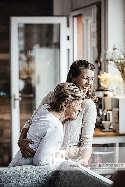 Cheerful young woman hugging grandmother while looking away