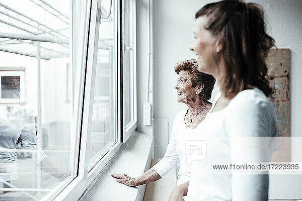 Glückliche Großmutter mit Enkelin  die durch das Fenster ihres Hauses schaut