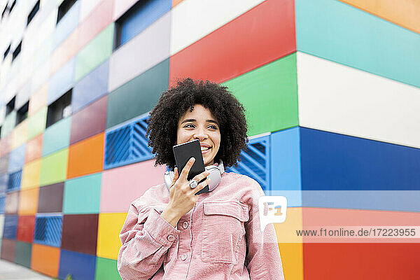 Young woman holding mobile phone in front of colorful building