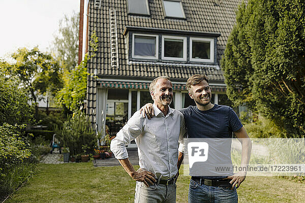 Lächelnder Sohn und Vater mit Hand auf der Hüfte im Hinterhof stehend an einem sonnigen Tag