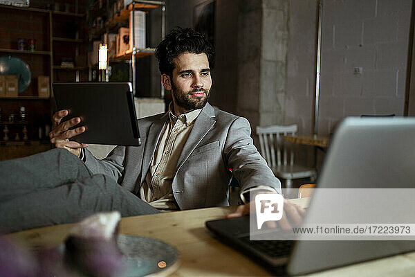 Gutaussehender männlicher Unternehmer mit digitalem Tablet  der in einem Café an einem Laptop arbeitet