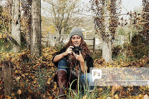 Lächelnde Frau  die durch die Kamera fotografiert  während sie mit ihrem Hund inmitten von Herbstblättern sitzt