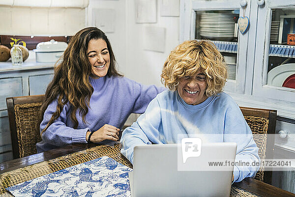 Mutter und Tochter lächelnd  während sie in der Küche auf einen Laptop schauen