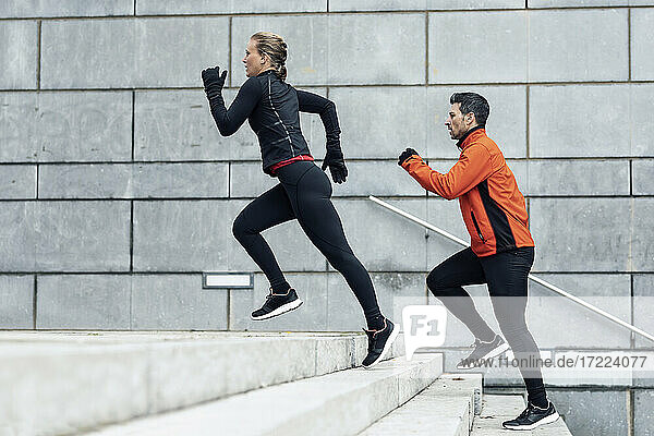 Sportlicher Mann und Frau laufen auf den Stufen an der Wand