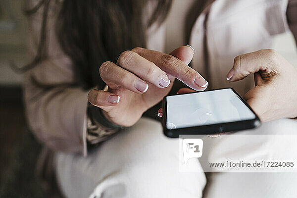 Hände einer Frau  die zu Hause ein Smartphone benutzt