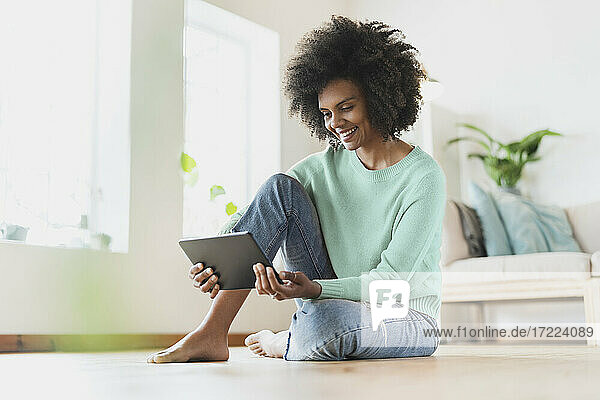 Junge Frau lächelt  während sie ein digitales Tablet zu Hause benutzt