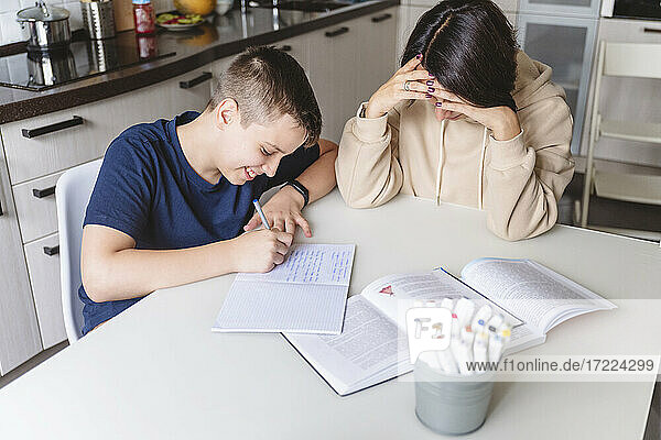 Frustrierte Mutter hilft ihrem Sohn bei den Hausaufgaben  während sie zu Hause am Esstisch sitzt