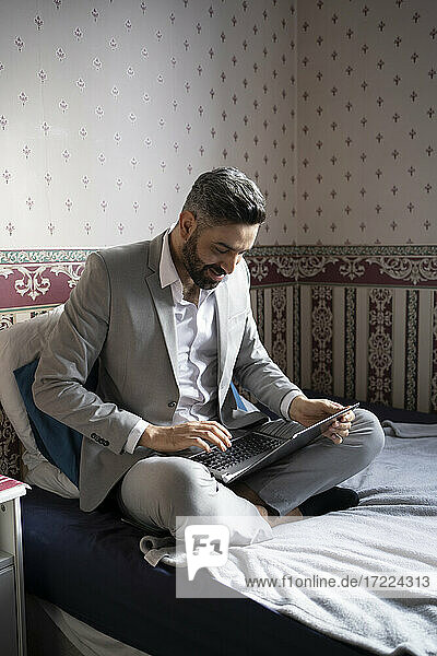 Lächelnder männlicher Unternehmer  der einen Laptop benutzt  während er von zu Hause aus arbeitet