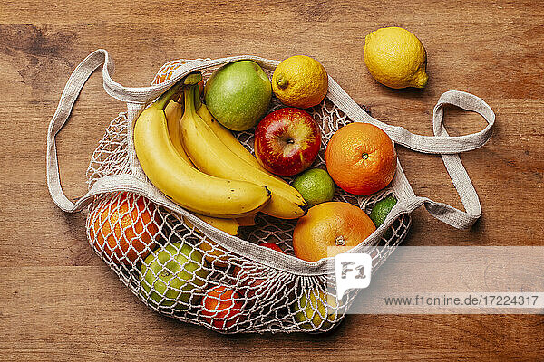 Wiederverwendbare Baumwoll-Netztasche mit frischen Früchten auf einem Holztisch liegend