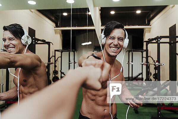 Fröhlicher Sportler mit Kopfhörern und Mobiltelefon  der einem Freund im Fitnessstudio die Faust gibt