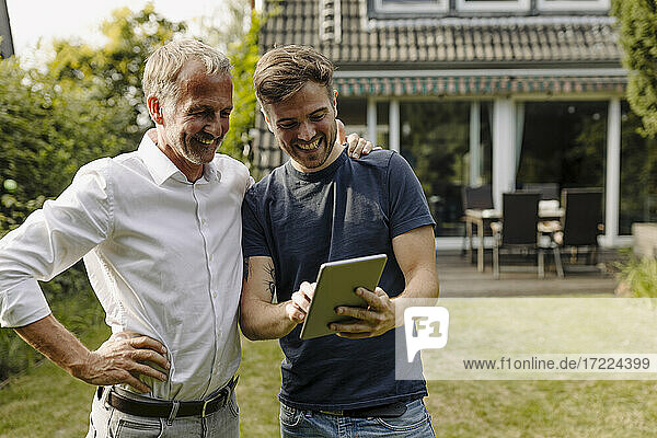Glücklicher Sohn benutzt ein digitales Tablet  während er neben seinem Vater im Hinterhof steht