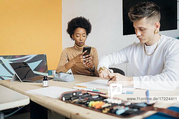 Young woman using smart phone while man working at table in studio
