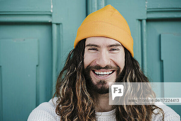 Cheerful male hipster wearing knit hat in front of door